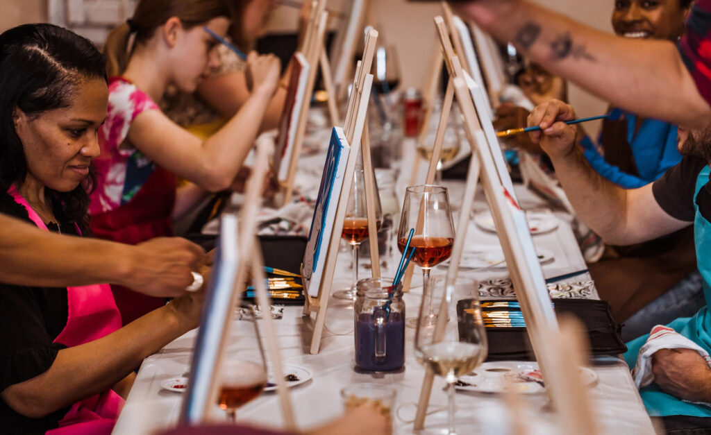 Grupo de personas pintando sobre lienzos durante una actividad creativa con vino