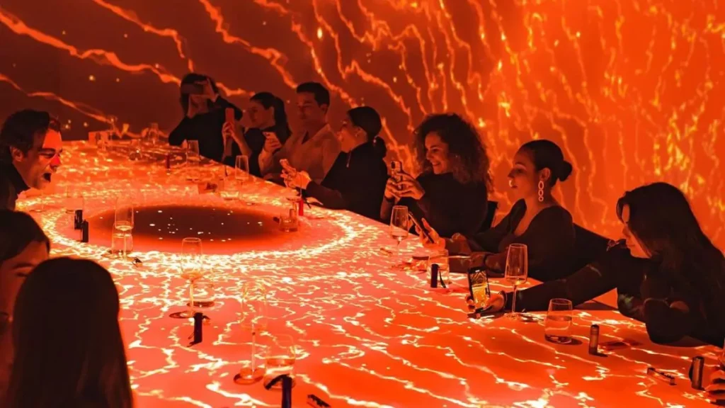 Grupo de personas disfrutando de una experiencia culinaria con efectos visuales naranjas proyectados sobre la mesa y las paredes