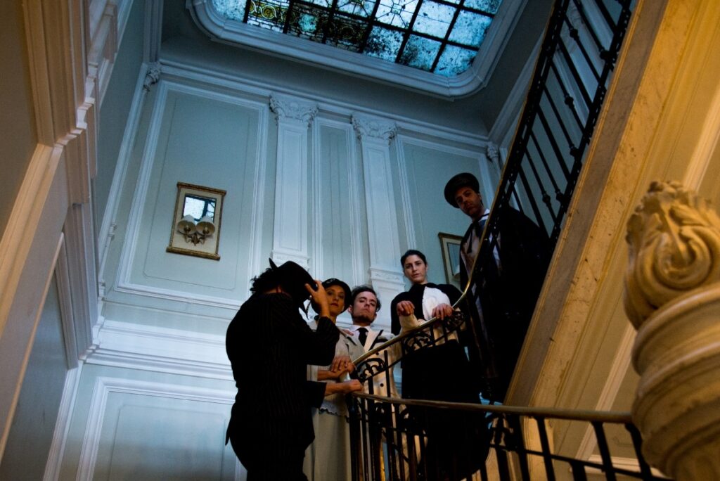 Grupo de personas elegantemente vestidas en una escalera de estilo clásico mirando hacia abajo