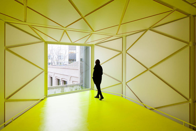 Persona en una sala de arquitectura contemporánea con tonos amarillos y líneas abstractas