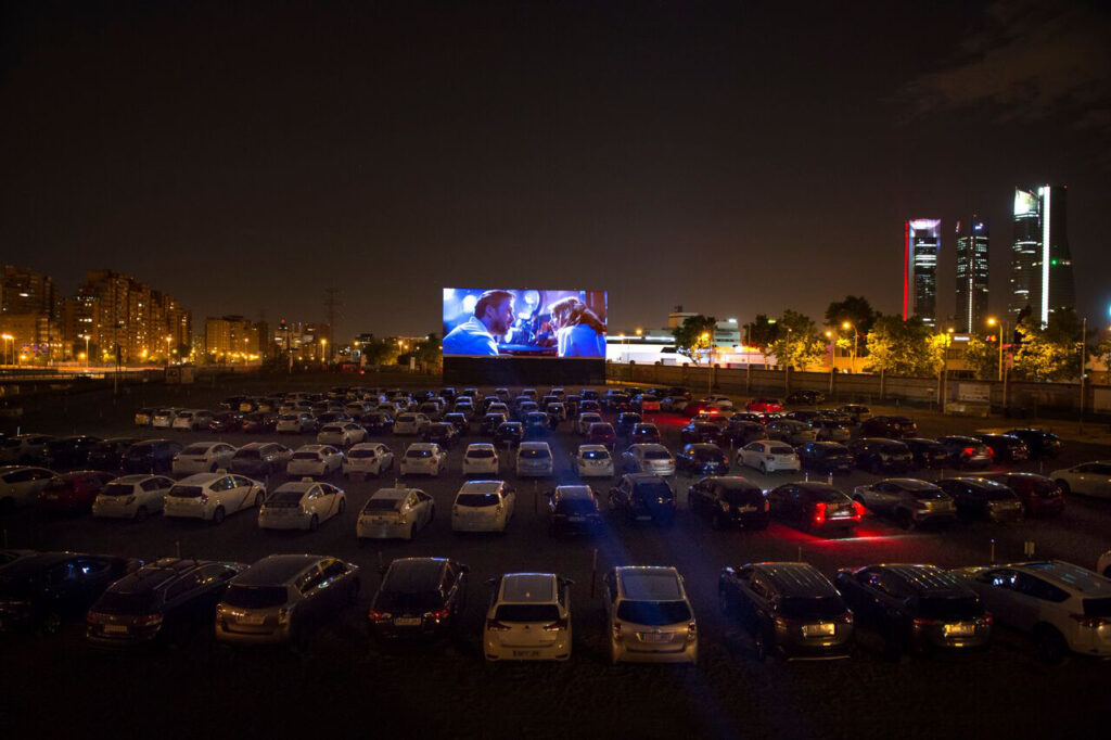 Autocine nocturno con coches frente a una gran pantalla de cine