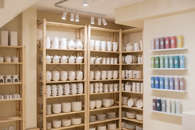 Taller de pintura de tazas con una estantería con las tazas para pintar en Madrid para días lluviosos