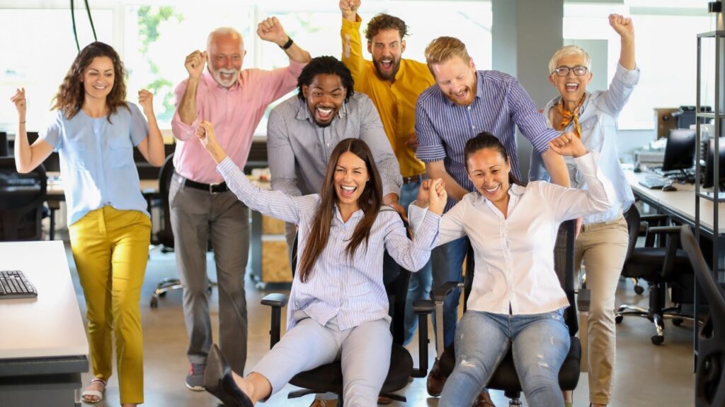 Equipo de profesionales diversos celebrando con los brazos en alto durante actividad de team building en oficina