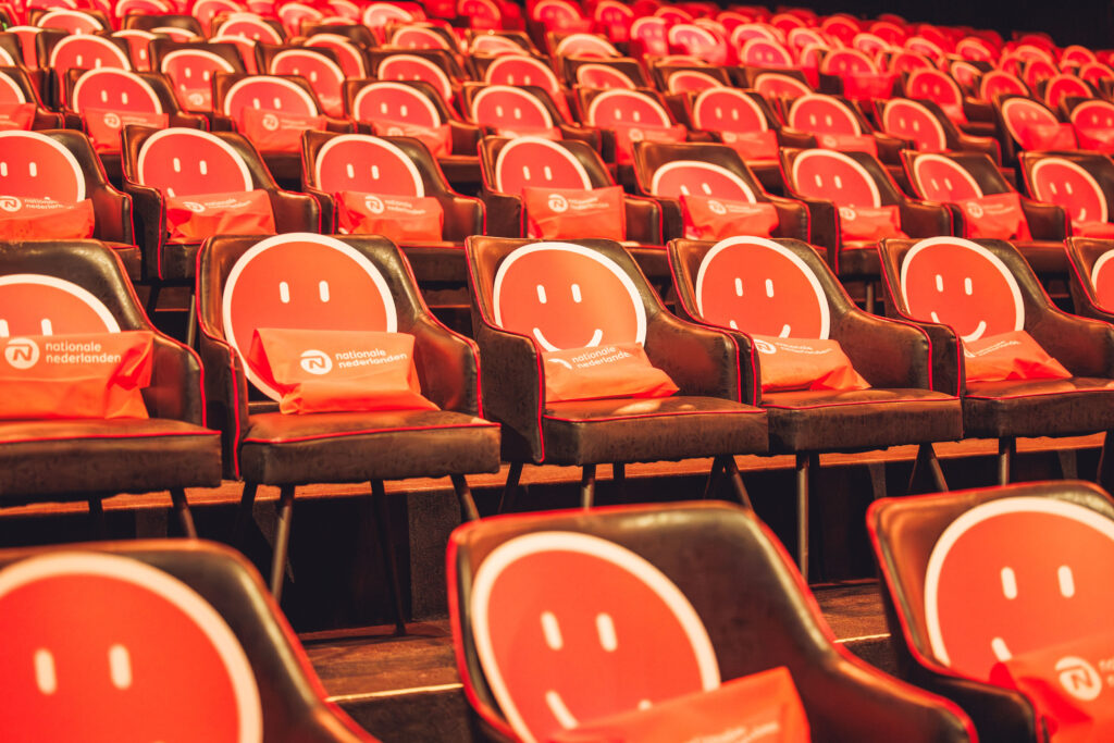 Auditorio vacío preparado para convención corporativa de Nationale Nederlanden con butacas decoradas con smiley face naranja y bolsas de bienvenida
