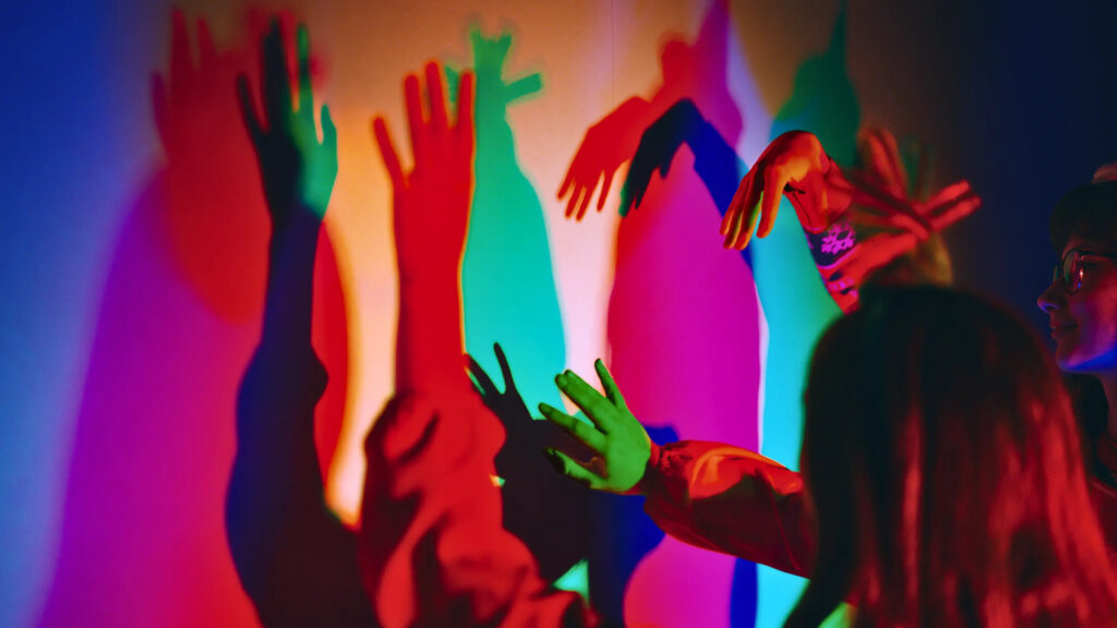 Personas interactuando con luces de colores y sombras proyectadas