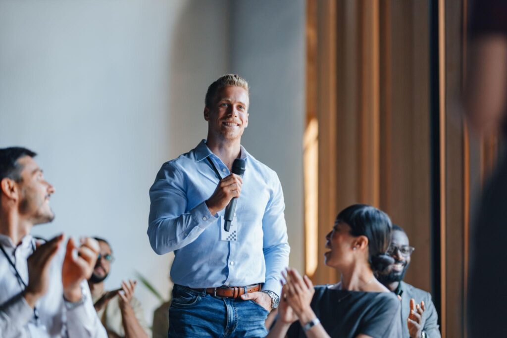 Asistente masculino con micrófono interviniendo entre aplausos durante sesión participativa de evento corporativo