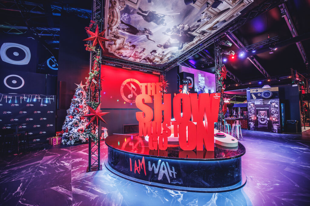 Food hall WAH con letras rojas gigantes 'The Show Must Go On' sobre escenario circular I Am WAH