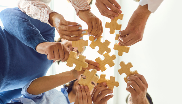 Grupo de compañeros uniendo piezas de puzzle de madera en equipo durante actividad de team building para motivar y conectar equipos