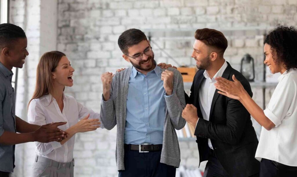 Equipo celebrando el logro de un compañero con aplausos en una oficina