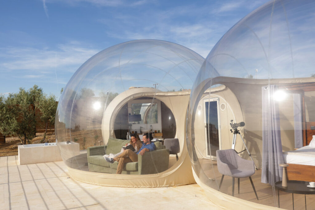 Pareja relajándose en un hotel burbuja transparente con salón y dormitorio, en una terraza soleada