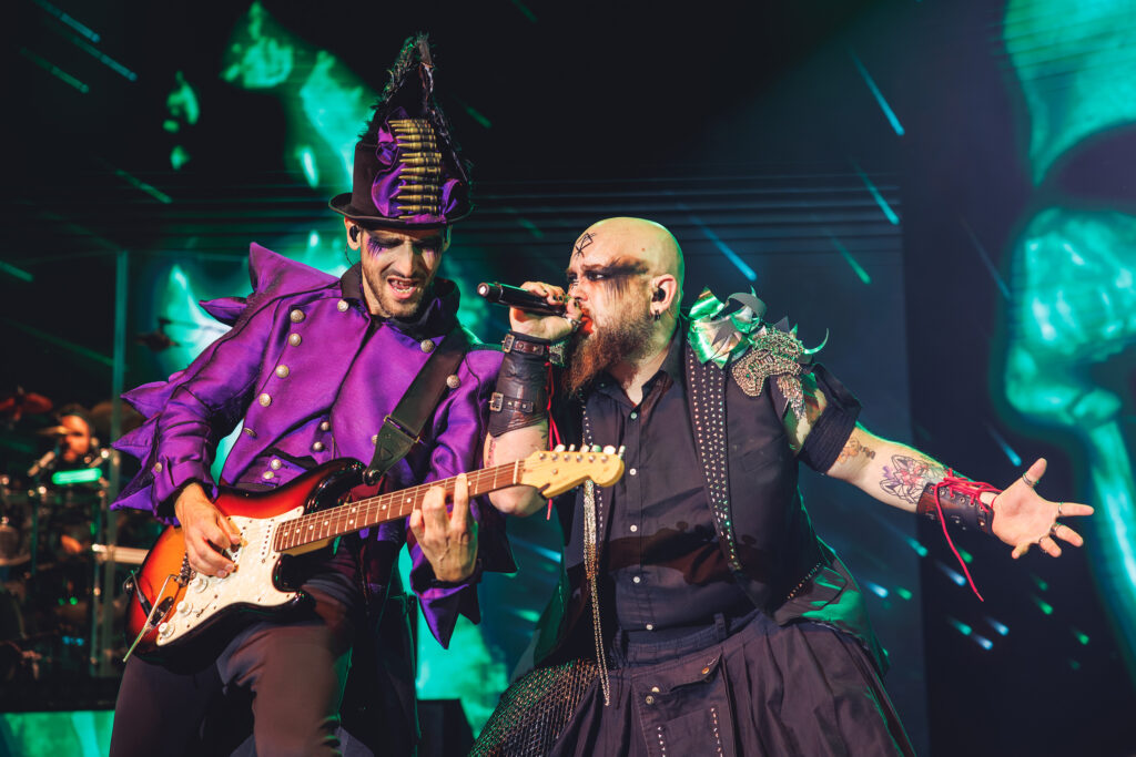 Primer plano de guitarrista y vocalista rock en el escenario de WAH, con iluminación verde y vestuario punk.