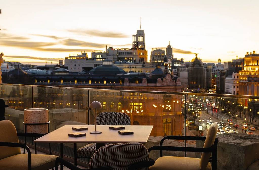 Vistas desde una terraza de diseño en Madrid al atardecer, con el Palacio de Cibeles y el Banco de España iluminados al fondo y una mesa preparada para dos en primer plano