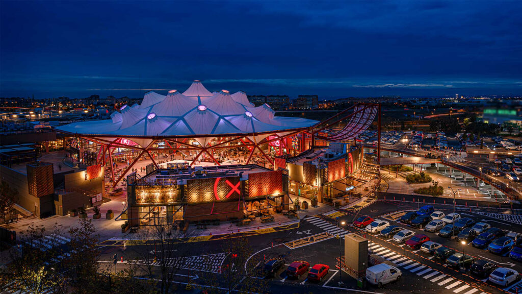 Panorámica de la fachada de X-Madrid, el centro de ocio extremo y comercial, con iluminación nocturna en tonos fríos y estructuras metálicas visibles