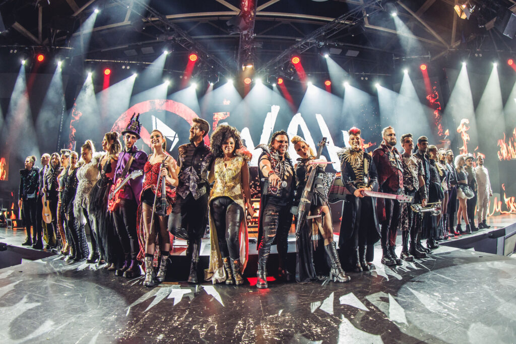 Elenco de WAH Show posando en el escenario; incluye bailaora de flamenco, cantantes de rock y músicos con instrumentos.