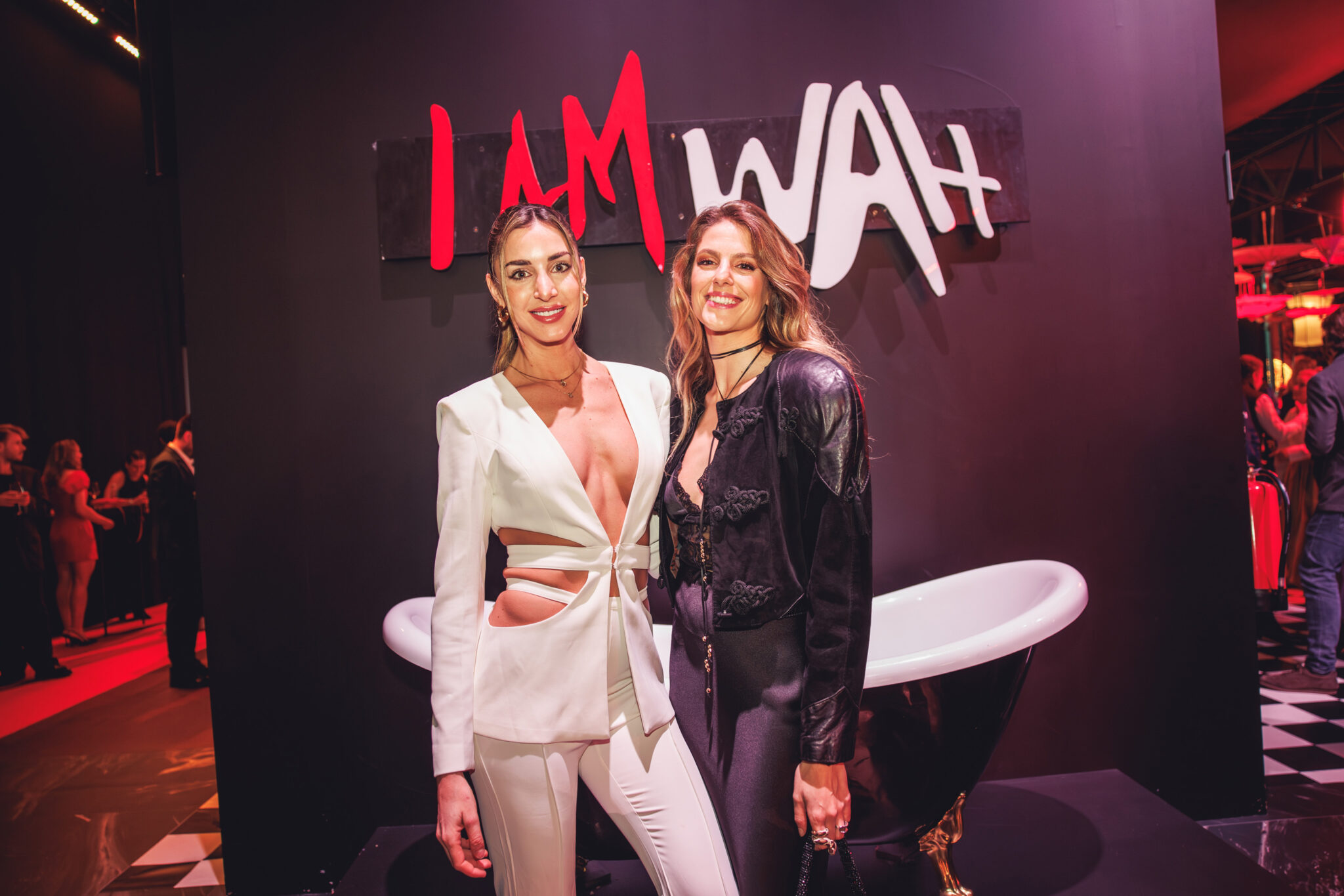 Dos invitadas posando en un photocall con una bañera clásica frente al letrero 'I AM WAH' en el recinto de WAH Madrid.