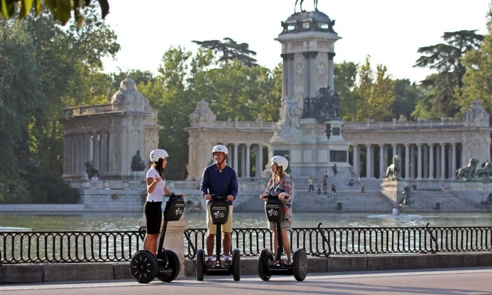 Tres personas con cascos en vehículos Segway frente al Monumento a Alfonso XII y el estanque del Parque del Retiro en Madrid